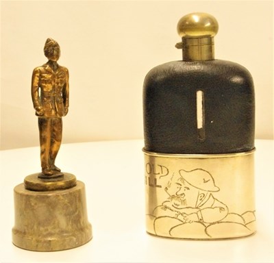 Lot 35 - A Bruce Bairnsfather 'Old Bill' hip flask. This glass flask, the top half covered in leather and bottom EPNS, is engraved with the WWI character. Also an early brass RAF officer mascot